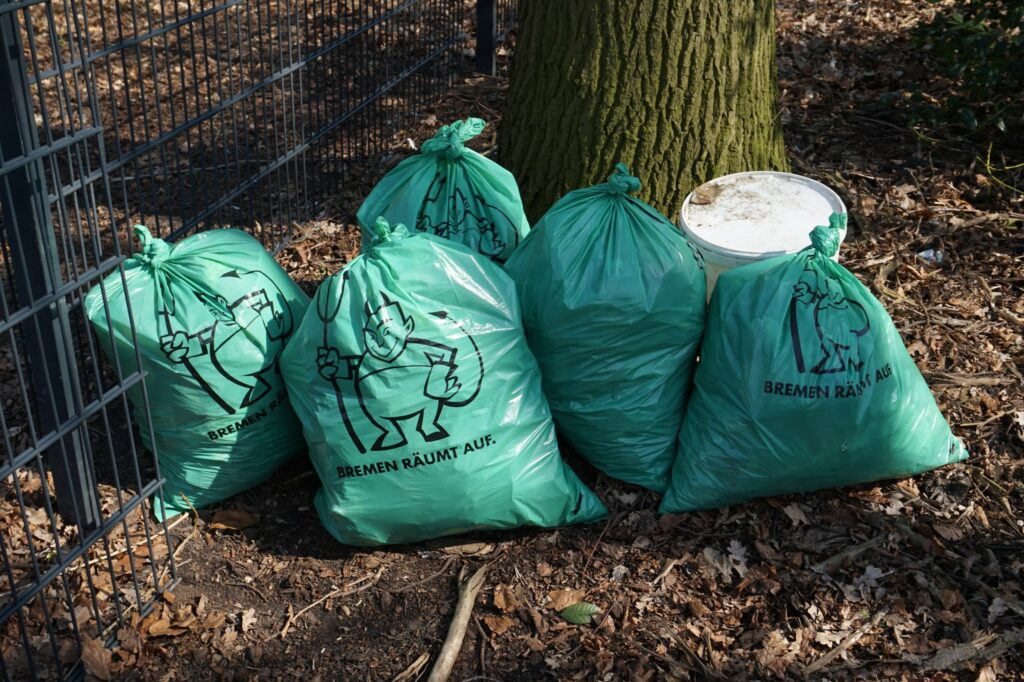 5 Müllsäcke, gefüllt mit Müll vor einem Baum